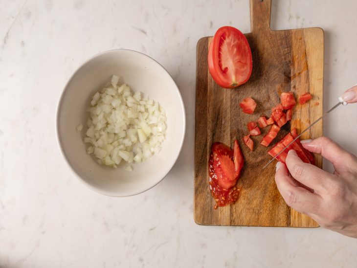 Uma tábua com o tomate picado e um recipiente com a cebola picada.