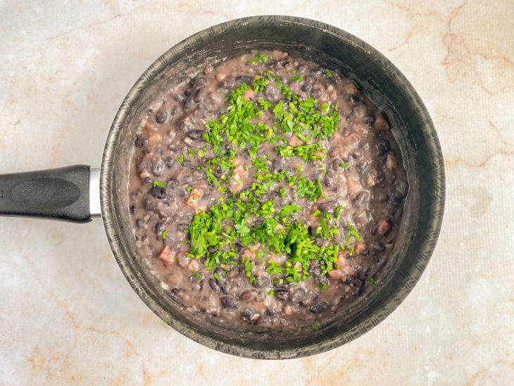 Feijão, farinha de mandioca e cheiro-verde adicionados e incorporados na frigideira com bacon.