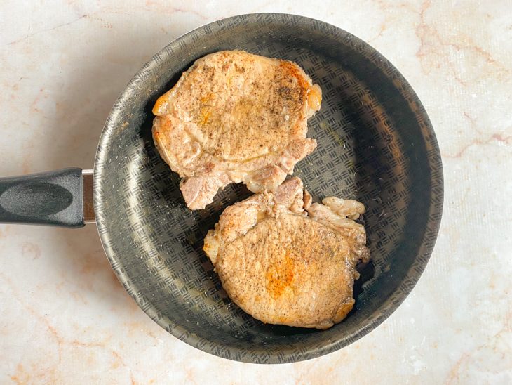 Bistecas suínas douradas em uma frigideira.