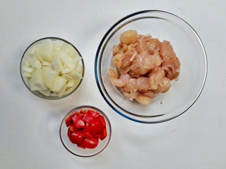 Cebola, pimentão e frango em cubos temperado, em recipientes distintos.