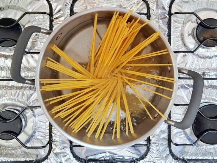 Macarrão cru adicionado na panela com água fervente.